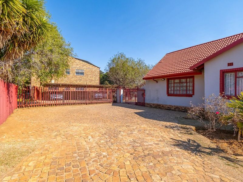 Front exterior view of the property featuring a cobblestone driveway, secure metal fencing, and a tiled roof house with security bars.