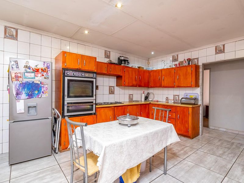 A functional kitchen featuring wooden cabinetry, a built-in double oven, hob, and tiled finishes throughout.