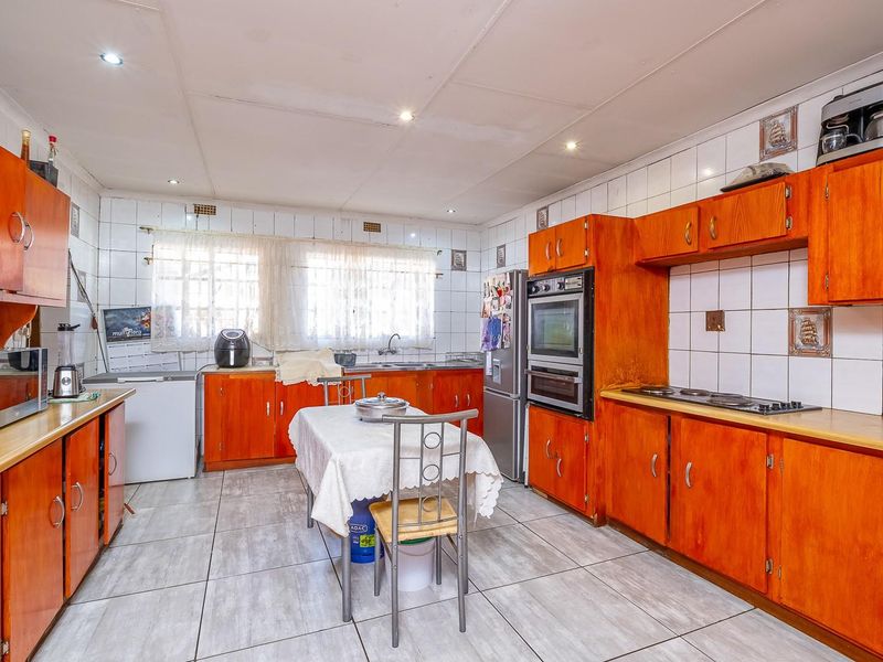 Spacious kitchen featuring extensive wooden cabinetry, built-in oven, hob, and tiled splashbacks, offering a functional layout with ample storage and preparation space.