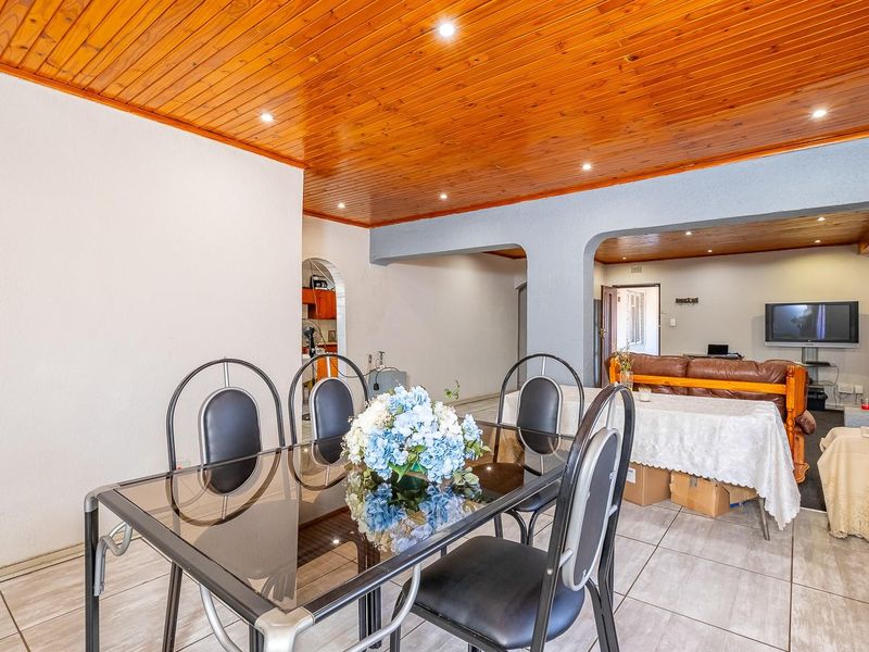 Open plan living and dining area featuring a warm timber tongue and groove ceiling, recessed lighting, and neutral ceramic floor tiles throughout.