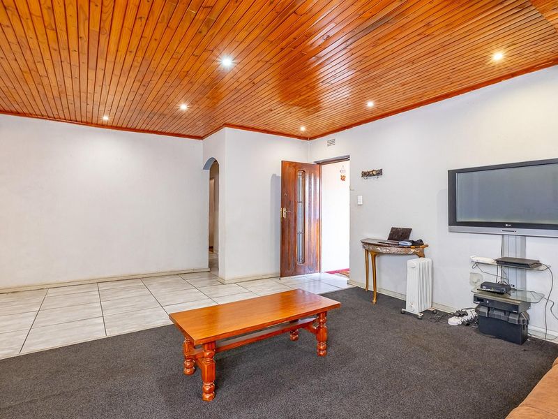 A living room featuring a timber tongue and groove ceiling, recessed downlights, and a combination of tiled and carpeted flooring.