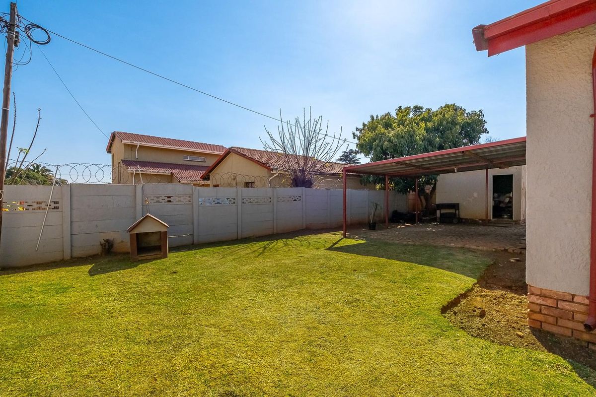Rear garden featuring a lawn, precast concrete boundary wall with razor wire, and a covered patio area.