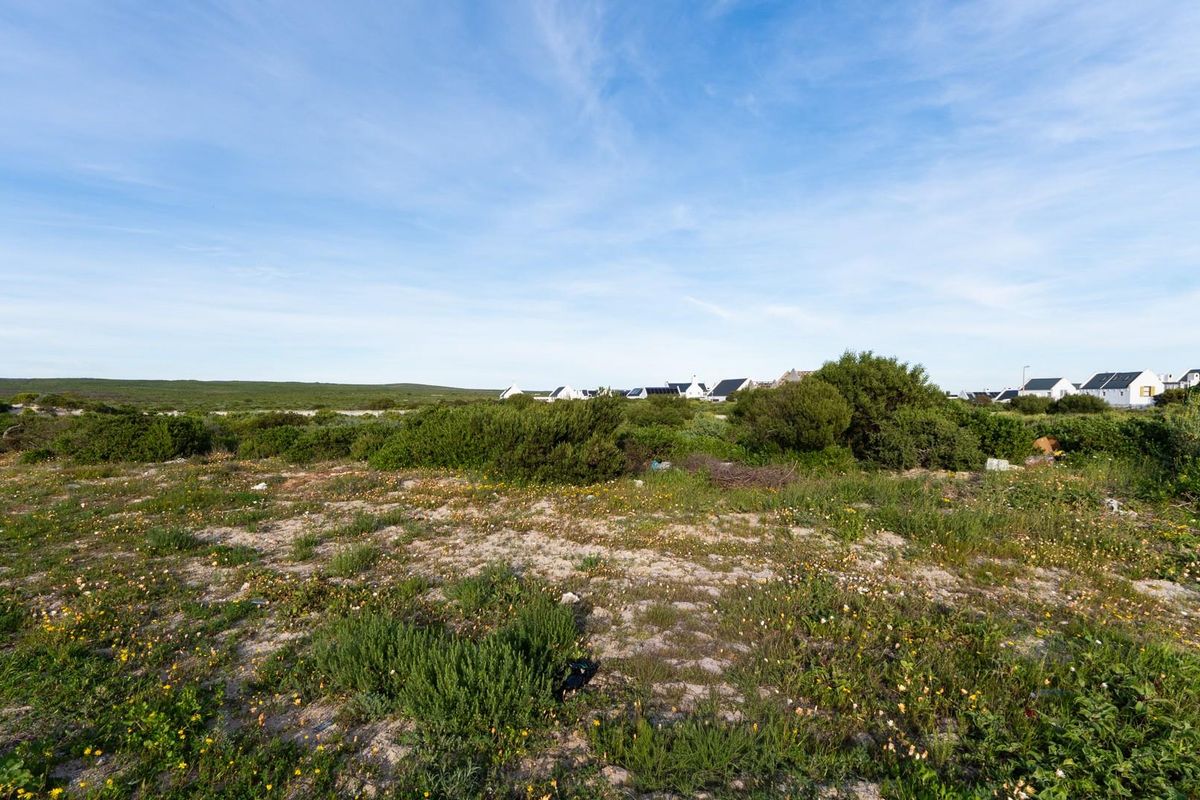 A view of a vacant residential plot featuring natural coastal vegetation and surrounding neighborhood homes in the distance.