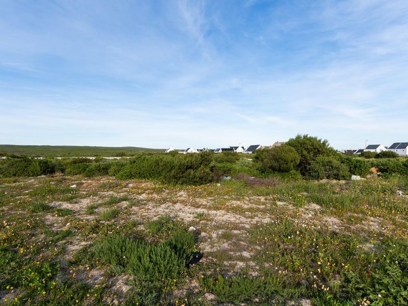 A view of a vacant residential plot featuring natural coastal vegetation and surrounding neighborhood homes in the distance.