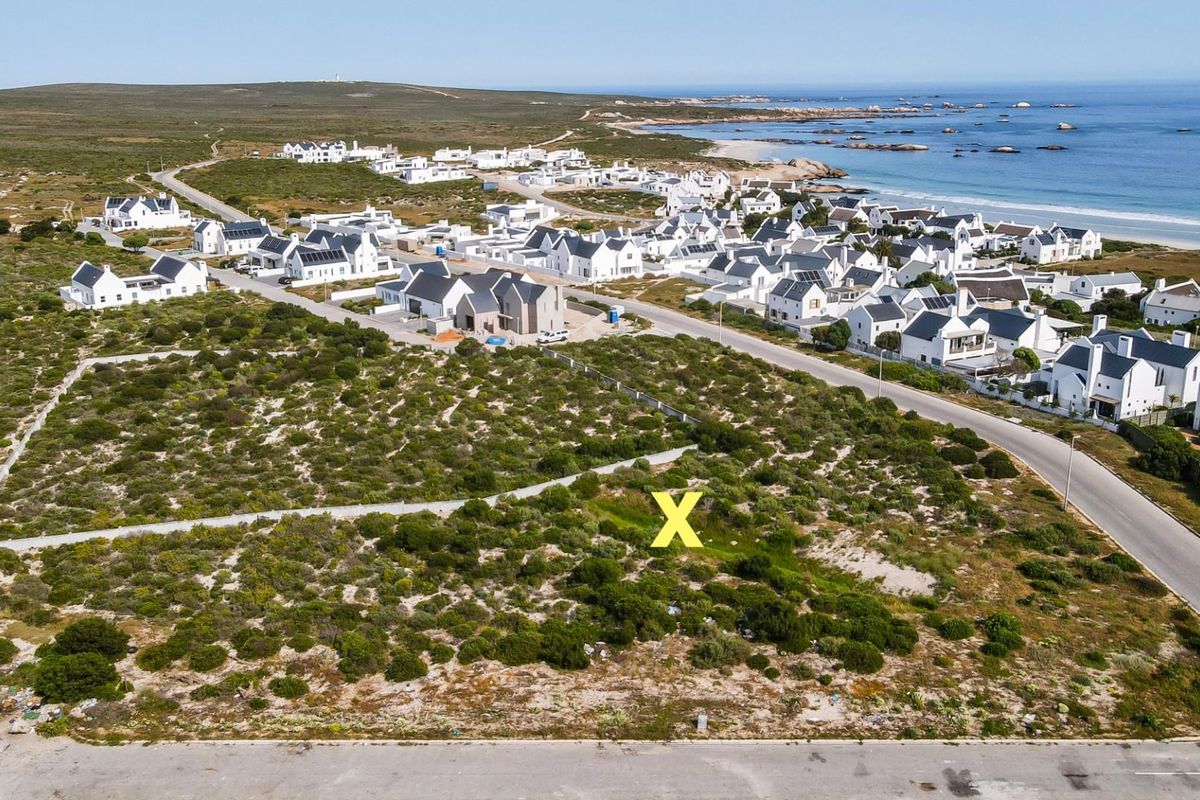 Aerial view of a vacant residential plot situated in a coastal estate, featuring natural vegetation and proximity to the beach and local infrastructure.