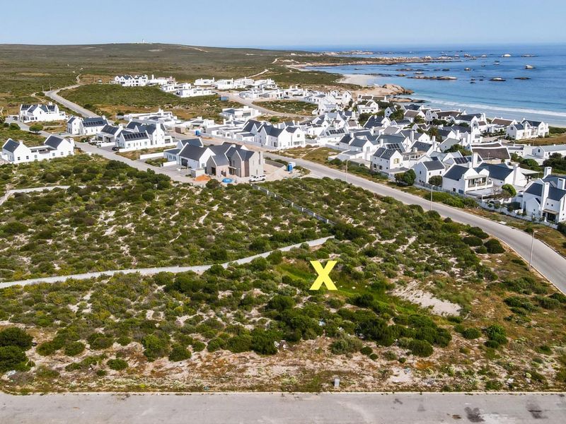 Aerial view of a vacant residential plot situated in a coastal estate, featuring natural vegetation and proximity to the beach and local infrastructure.