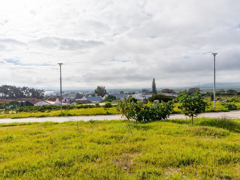 A scenic view overlooking a residential neighborhood from a vacant plot of land, featuring established street lighting and paved road access.