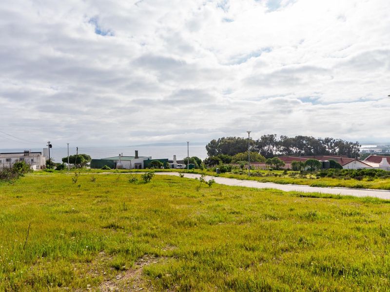 A view of a vacant residential plot featuring established street infrastructure, paved access, and distant coastal scenery.