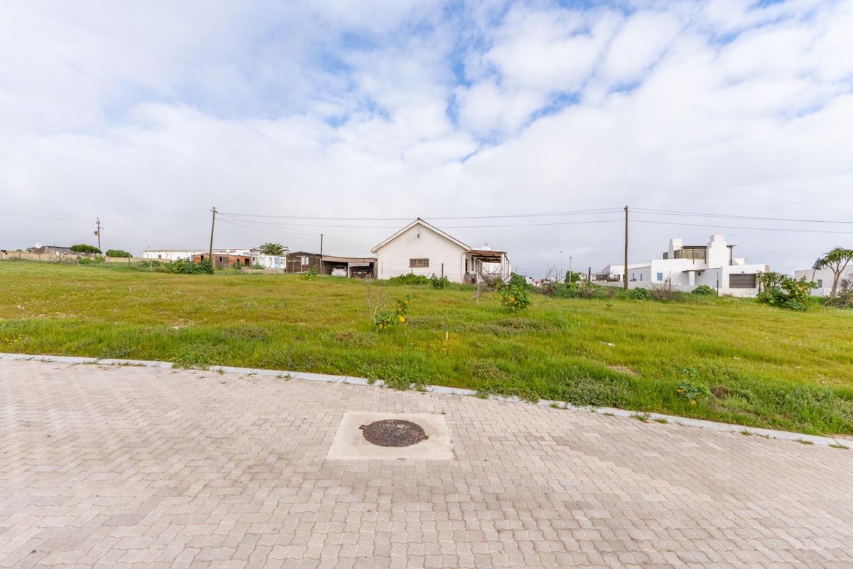 A view of a vacant residential plot featuring a paved driveway, utility access, and surrounding neighborhood infrastructure.