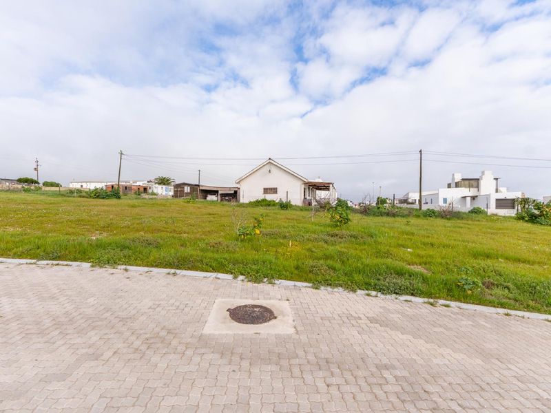 A view of a vacant residential plot featuring a paved driveway, utility access, and surrounding neighborhood infrastructure.
