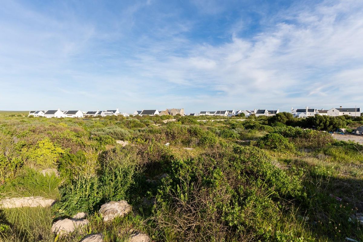 A wide-angle view of a vacant residential plot featuring natural coastal vegetation with established residential properties visible in the distance.