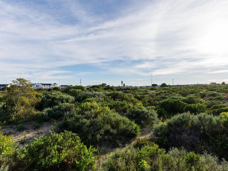 A view of a vacant residential plot featuring natural coastal vegetation and sandy terrain, suitable for future development.