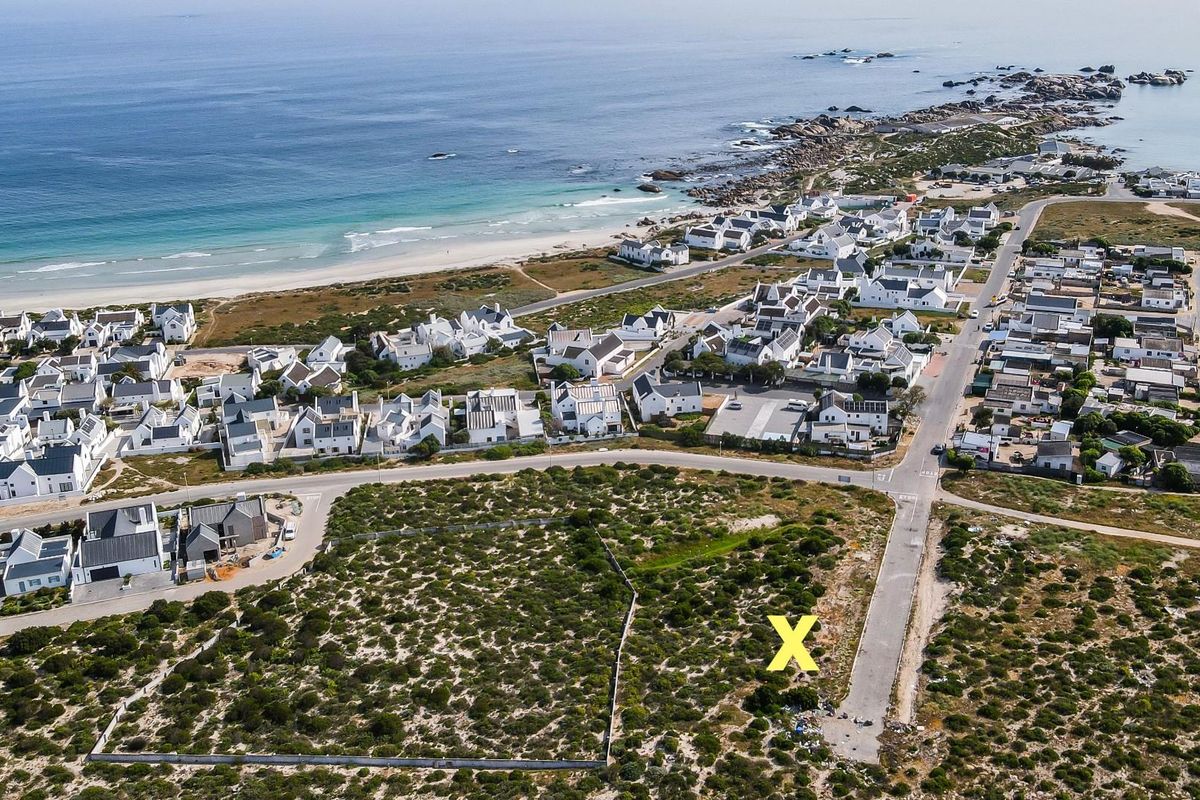 Aerial view of a vacant residential plot located in a coastal development, featuring road access and proximity to the beach.