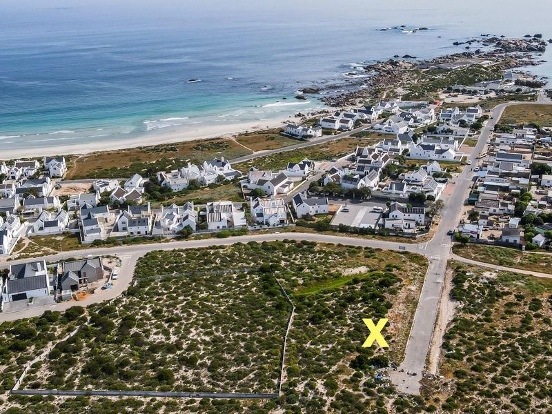 Aerial view of a vacant residential plot located in a coastal development, featuring road access and proximity to the beach.