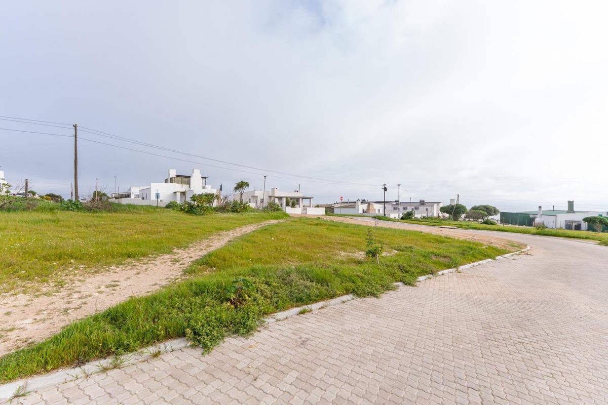 A vacant residential plot featuring a grassy landscape, adjacent to a paved street with established utility infrastructure in a suburban setting.