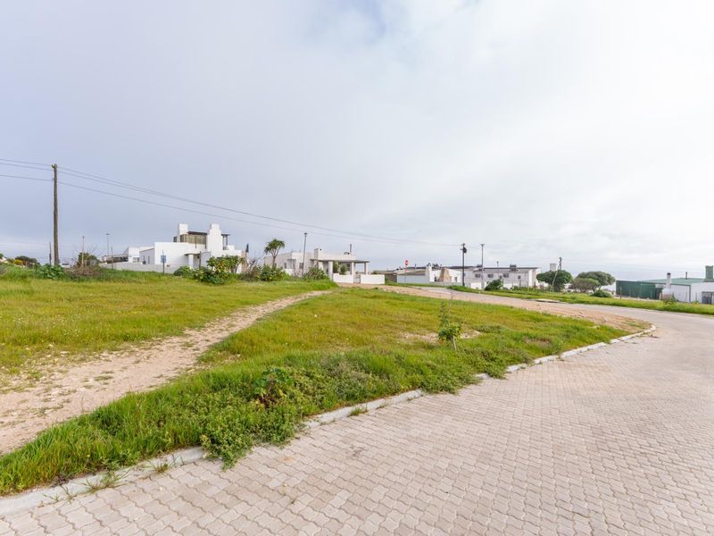A vacant residential plot featuring a grassy landscape, adjacent to a paved street with established utility infrastructure in a suburban setting.