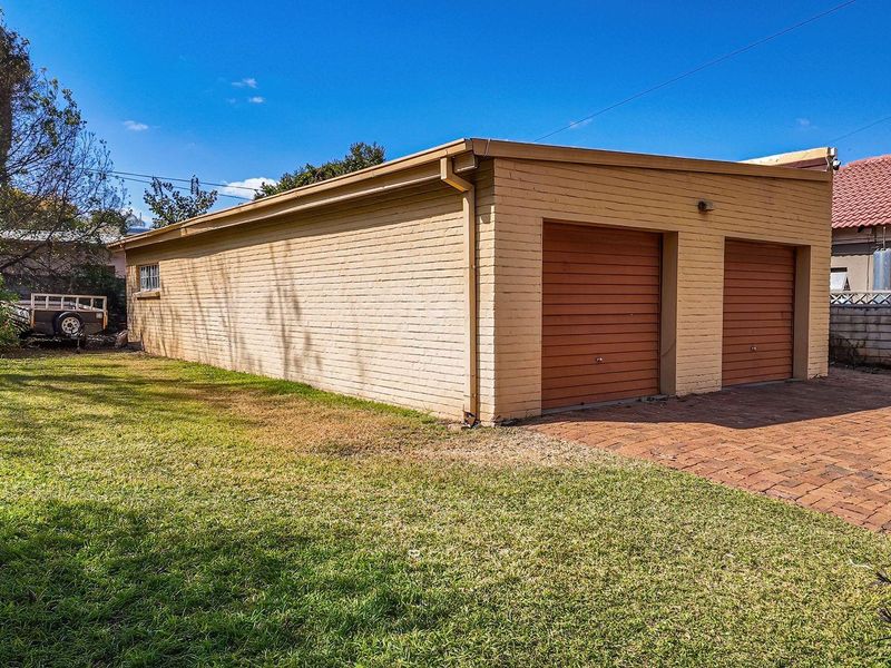 A detached double garage with brick exterior and roller doors, situated on a paved driveway with adjacent lawn area.