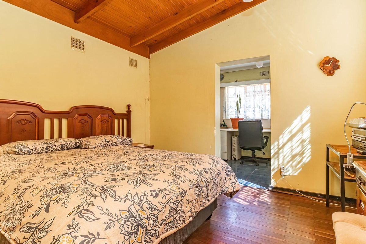 Spacious bedroom featuring exposed timber ceiling beams, timber flooring, and an adjoining study area with natural light.