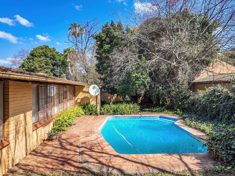 Outdoor pool area featuring a swimming pool with brick paving, adjacent to the rear building elevation with security bars on windows.