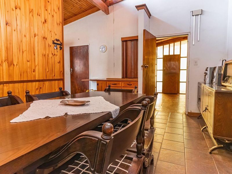 Dining area featuring timber wall paneling, exposed ceiling beams, and tiled flooring, leading to an entrance hallway with natural light.