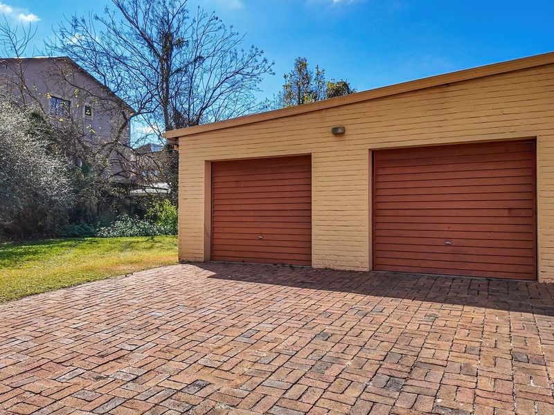 A detached double garage featuring brick construction and a paved driveway, set within a residential garden area.