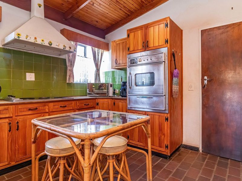 A dated kitchen featuring timber cabinetry, a built-in oven, extractor fan, green tiled backsplash, and traditional tiled flooring under a timber ceiling.