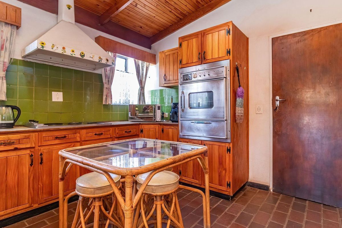 A dated kitchen featuring timber cabinetry, a built-in oven, extractor fan, green tiled backsplash, and traditional tiled flooring under a timber ceiling.