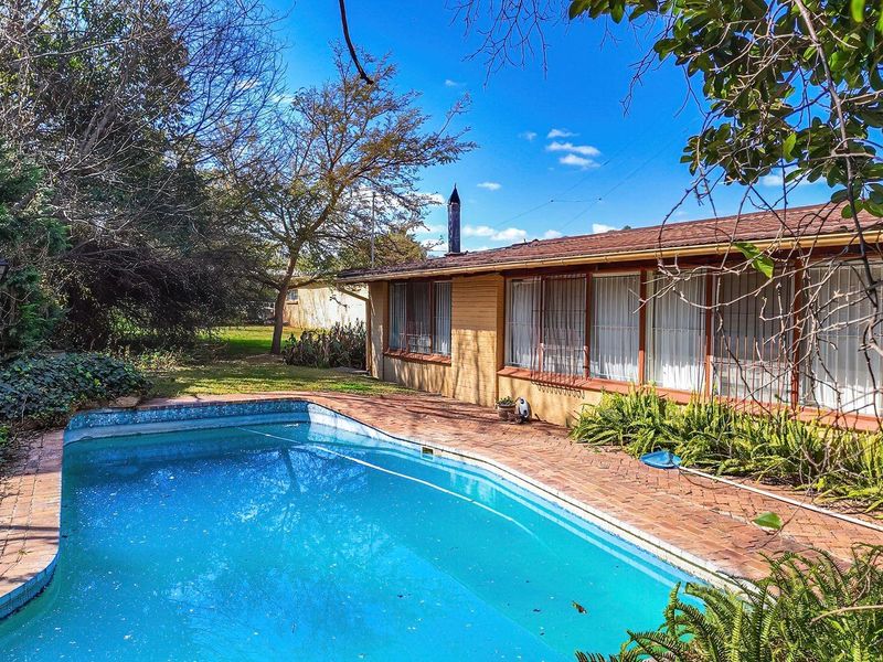 A backyard view featuring a swimming pool with brick paving and a single-story house exterior with a tiled roof.