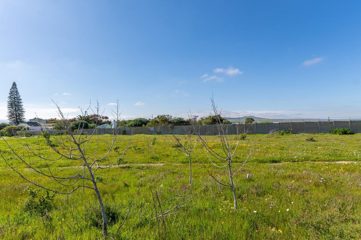A vacant residential plot featuring open grassy terrain, perimeter walling, and security fencing, offering a clear space for future development.