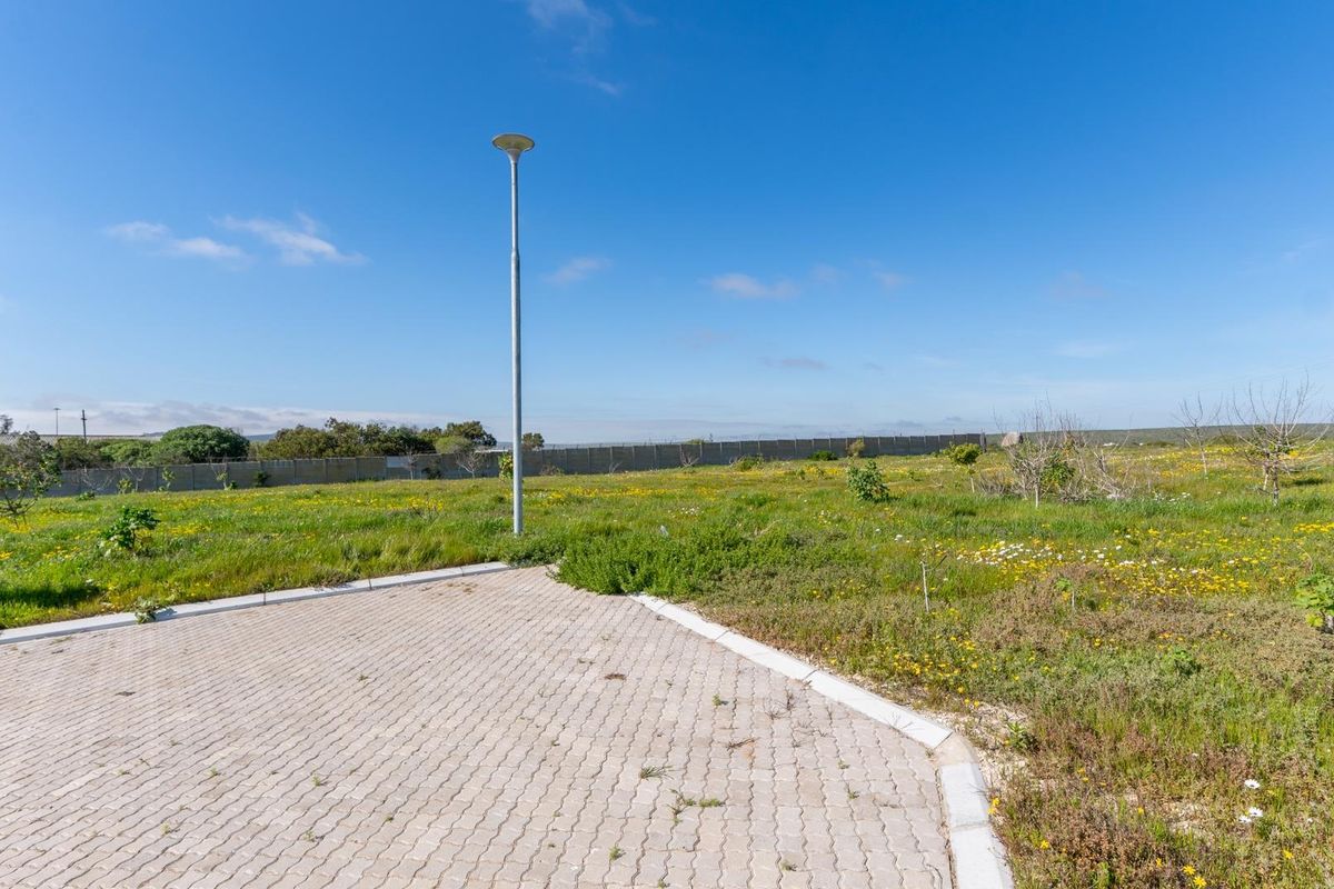 A vacant residential plot featuring a paved driveway section, a street light, and perimeter walling, surrounded by natural vegetation.