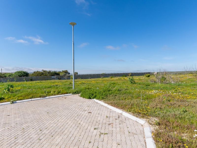 A vacant residential plot featuring a paved driveway section, a street light, and perimeter walling, surrounded by natural vegetation.