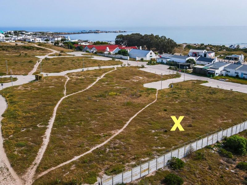 Aerial view of a vacant residential plot situated in a coastal estate, featuring established access roads and perimeter fencing.