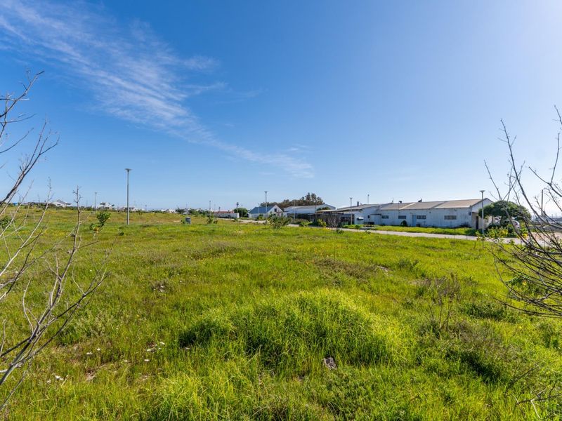 A wide-angle view of a vacant residential plot featuring natural grass coverage and existing street lighting infrastructure in a suburban setting.