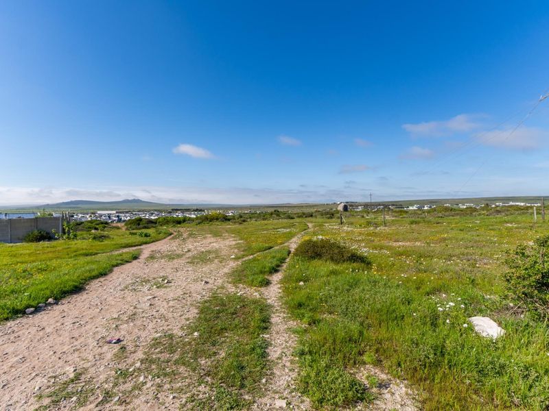 A vacant residential plot featuring natural vegetation, a dirt access path, and distant views of the surrounding landscape.