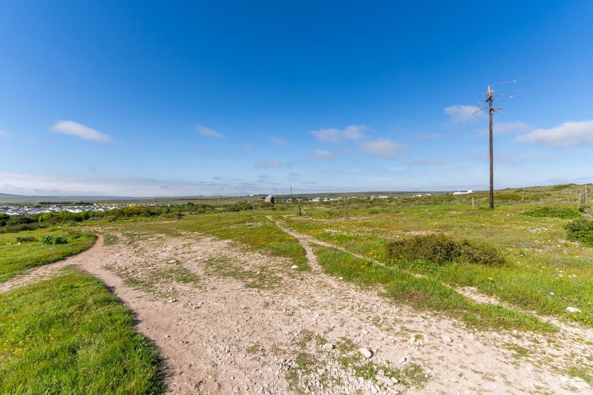 An elevated view of a vacant residential plot featuring natural vegetation, an unpaved access track, and an existing utility pole with overhead power lines.