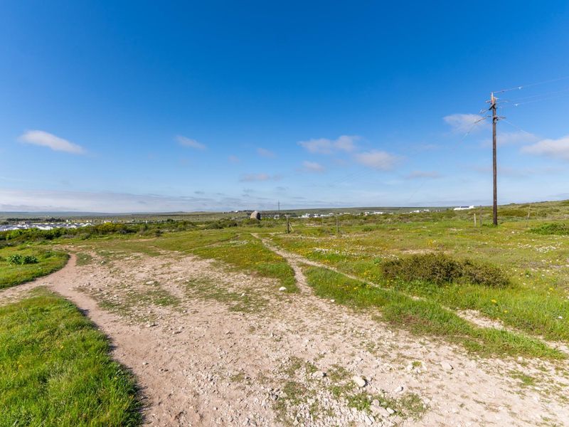 An elevated view of a vacant residential plot featuring natural vegetation, an unpaved access track, and an existing utility pole with overhead power lines.
