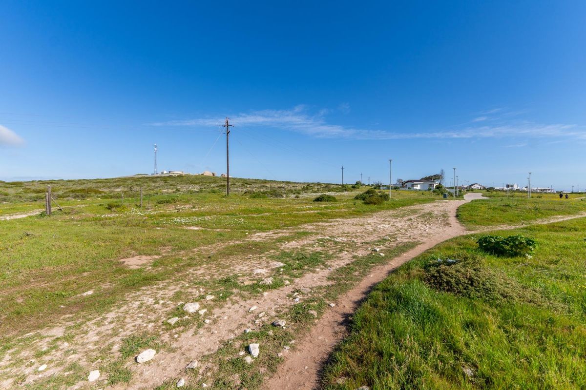 A wide-angle view of a vacant residential plot featuring natural vegetation, a dirt access path, and existing utility infrastructure.