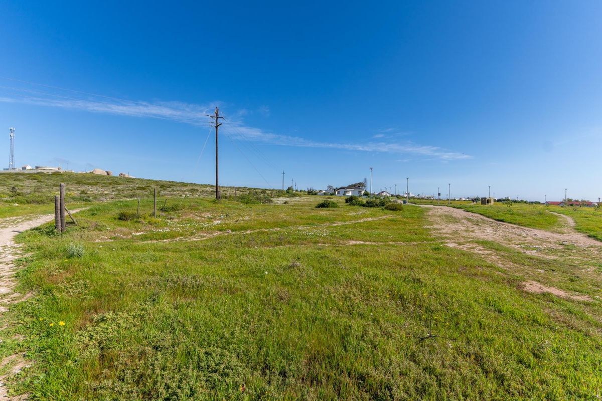 A wide-angle view of a vacant residential plot featuring natural grass cover, utility poles, and an unpaved access track.