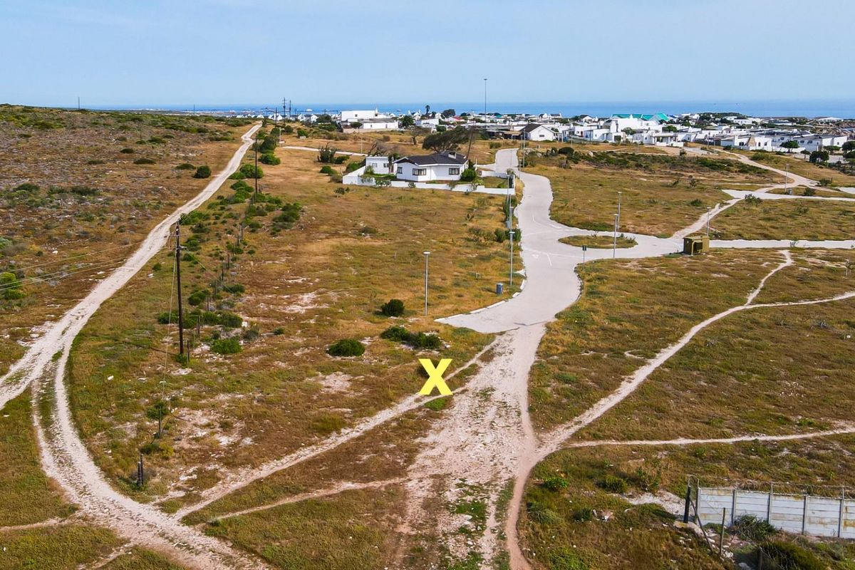 Aerial view of a vacant residential plot featuring established road access, utility infrastructure, and proximity to the coastal neighborhood.