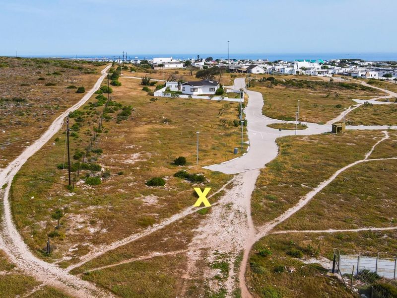 Aerial view of a vacant residential plot featuring established road access, utility infrastructure, and proximity to the coastal neighborhood.