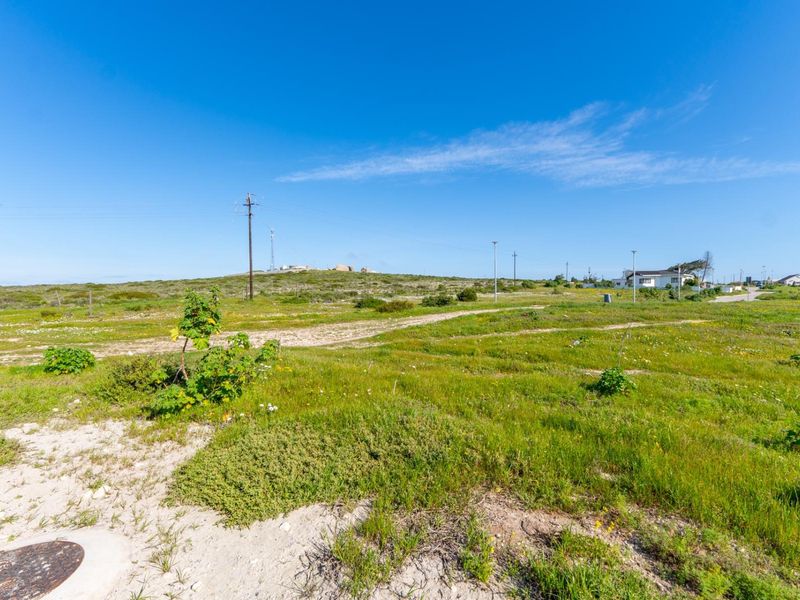 A vacant residential plot featuring natural vegetation, utility infrastructure, and clear views of the surrounding landscape.