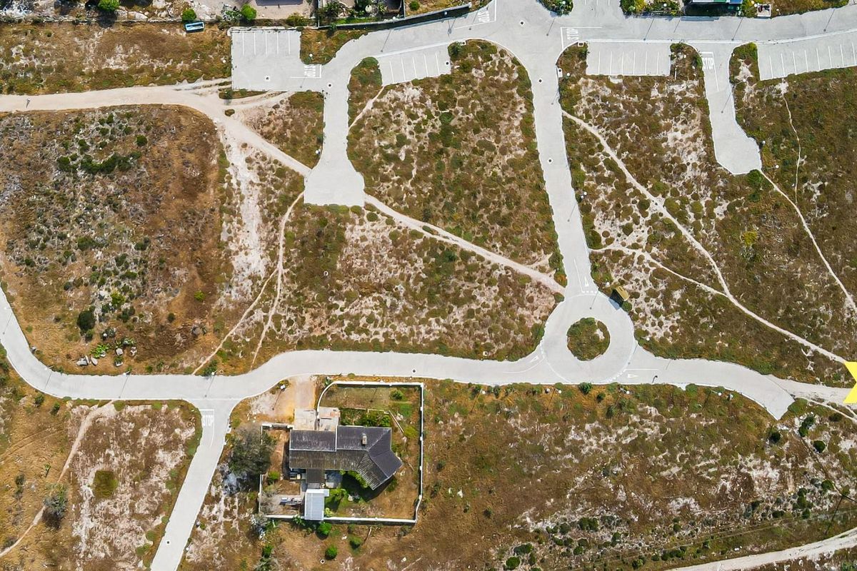 Aerial view of a residential development site featuring paved roads, a cul-de-sac, parking areas, and an existing property with boundary walls.