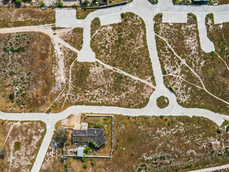 Aerial view of a residential development site featuring paved roads, a cul-de-sac, parking areas, and an existing property with boundary walls.