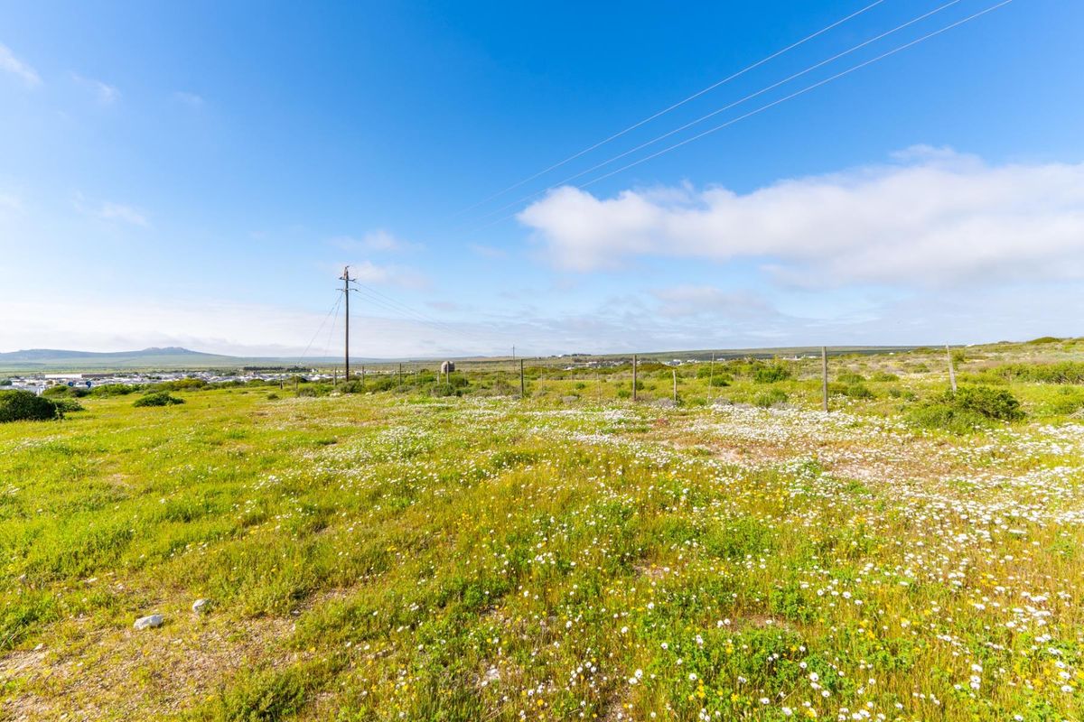 A wide-angle view of a vacant residential plot featuring natural vegetation, wire fencing, and utility infrastructure under a clear blue sky.