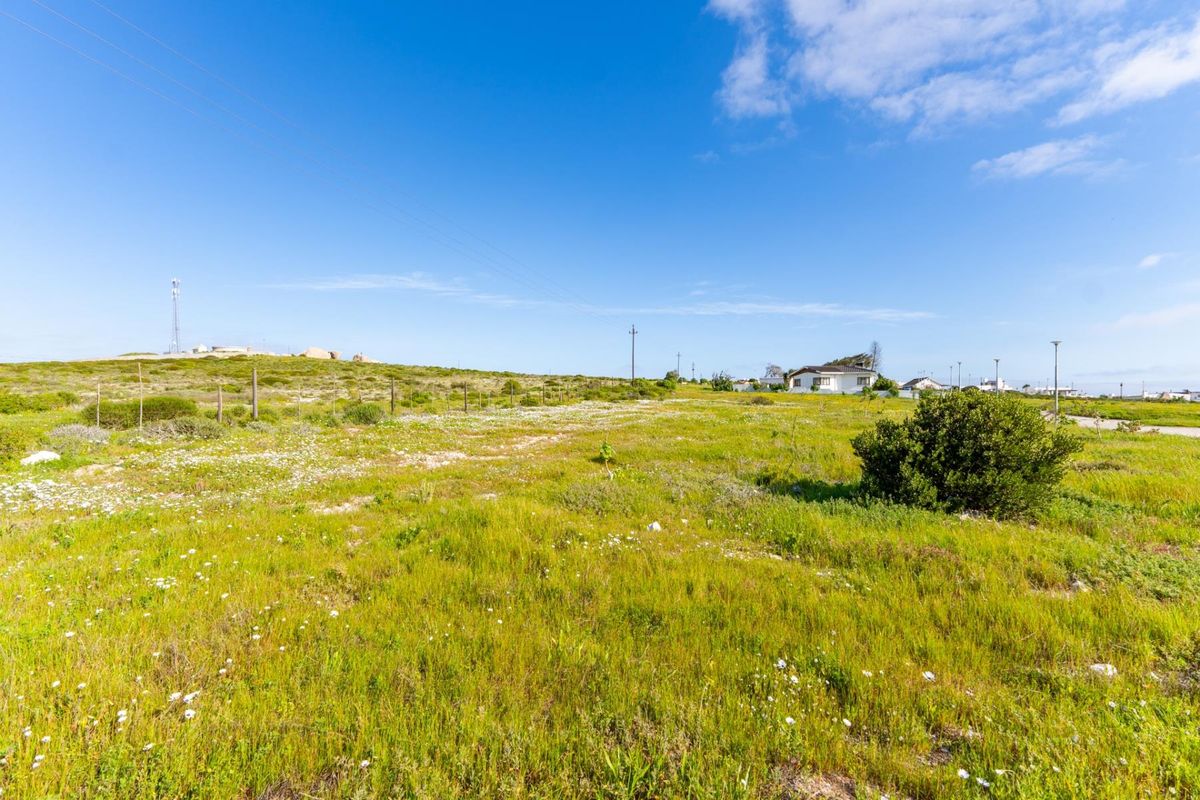 A vacant residential plot featuring natural grass coverage, perimeter wire fencing, and overhead utility lines under a clear blue sky.