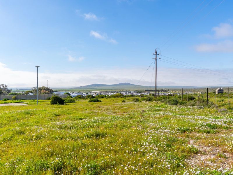A wide-angle view of a vacant residential plot featuring natural vegetation, perimeter fencing, and distant mountain views.