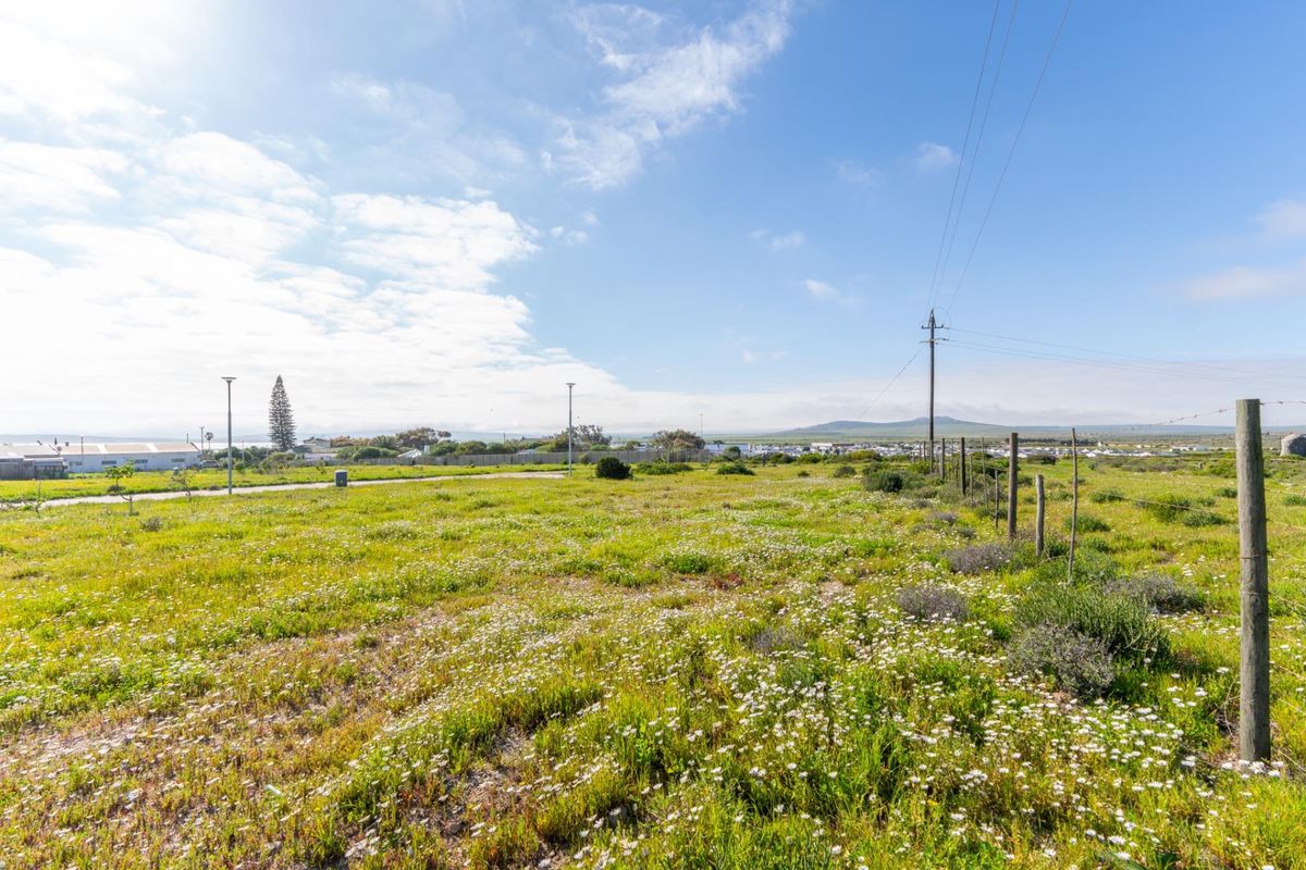 A vacant residential plot featuring natural vegetation, wire fencing, and existing utility infrastructure, offering a clear view of the surrounding landscape.