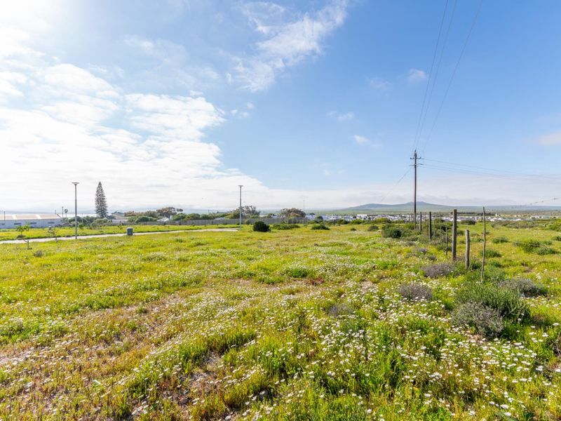 A vacant residential plot featuring natural vegetation, wire fencing, and existing utility infrastructure, offering a clear view of the surrounding landscape.
