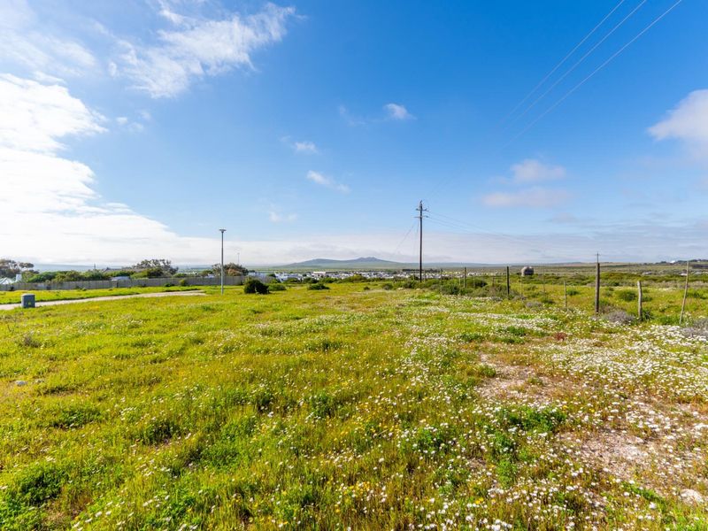 A vacant residential plot featuring natural vegetation, wire fencing, and utility infrastructure with distant landscape views.