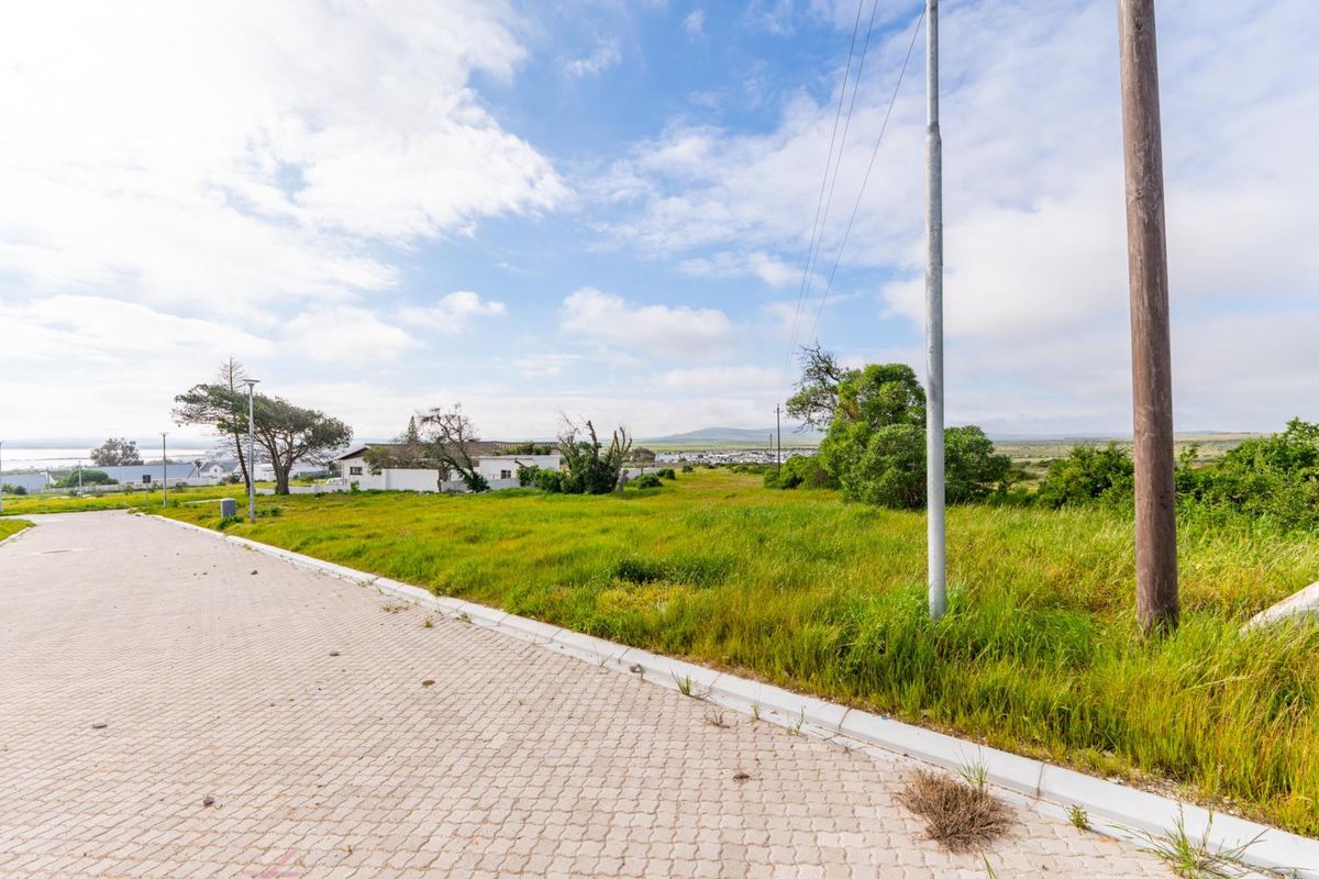 A street-level view of a vacant residential plot featuring paved road access, concrete curbing, and existing utility infrastructure.